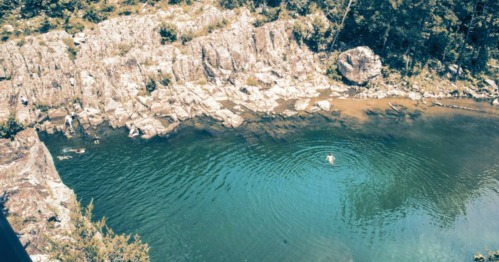 Aerial view of a serene swimming hole surrounded by rocky cliffs and lush greenery.