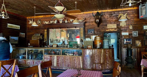 Interior of a rustic bar with wooden decor, vintage items, and animal mounts on the walls. Tables with checkered cloths.