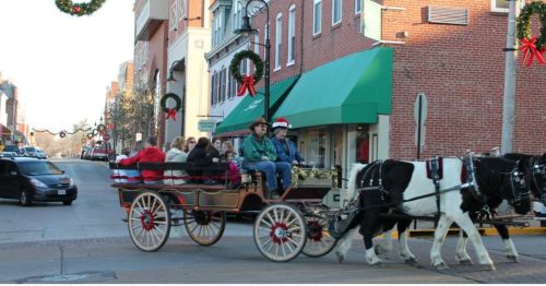 A horse-drawn carriage with passengers rides through a festive street decorated for the holidays.