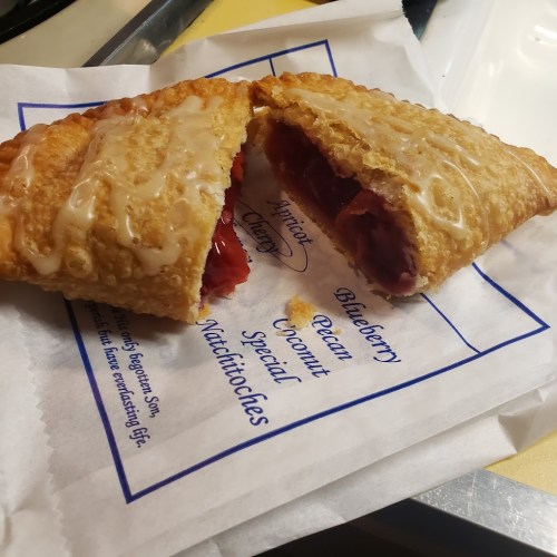 A flaky pastry filled with blueberry filling, drizzled with icing, resting on a paper with flavor options listed.