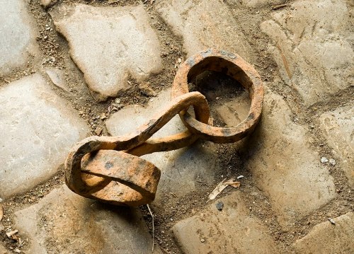 An old, rusted metal chain link lying on a cobblestone surface with dirt around it.