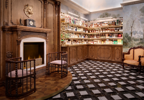 A cozy, elegant room with a fireplace, wooden shelves filled with bottles, and stylish seating.