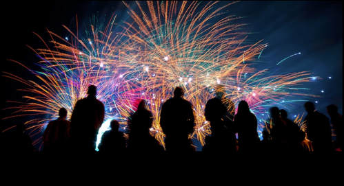 Silhouettes of people watching a vibrant fireworks display against a dark sky.