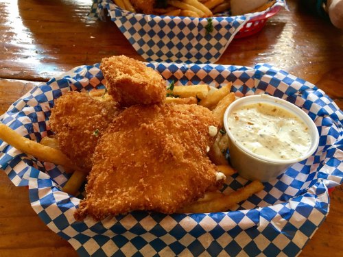 A basket of golden fried fish fillets served with crispy fries and a side of dipping sauce.