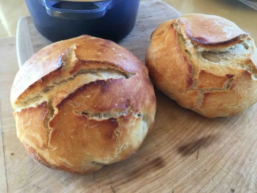 Two round, crusty loaves of bread with golden-brown tops, resting on a wooden cutting board.