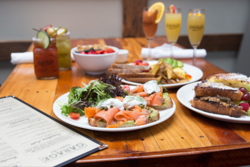 A table set with various brunch dishes, including smoked salmon, salads, and drinks, alongside a menu.