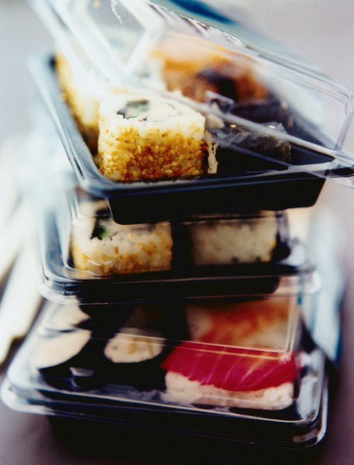 A stack of sushi containers, each filled with various types of sushi rolls, neatly arranged and covered.