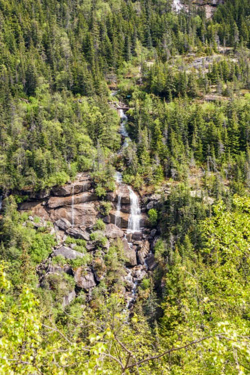 A cascading waterfall flows down a rocky cliff, surrounded by lush green trees and vibrant foliage.