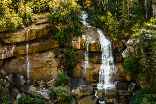 A scenic view of two waterfalls cascading down rocky cliffs, surrounded by lush green trees and foliage.