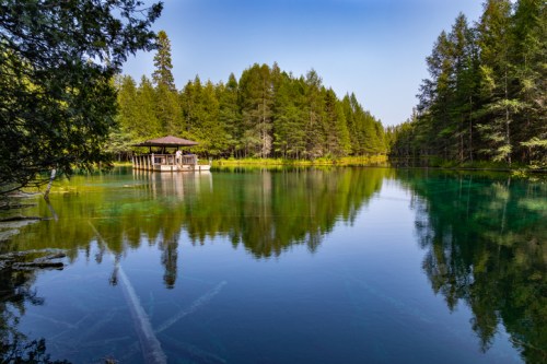 A serene lake surrounded by lush trees, featuring a small wooden pavilion on the water's edge.
