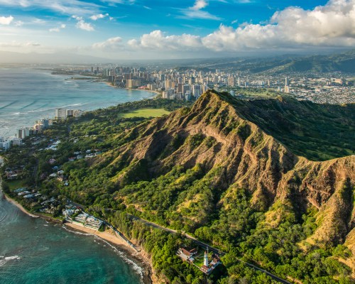 Aerial view of Diamond Head crater with Honolulu skyline and coastline in the background under a blue sky.