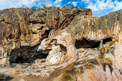 Rocky landscape featuring textured cliffs and caves under a blue sky with scattered clouds.