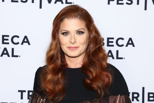 A woman with long, wavy red hair smiles at the Tribeca Festival, wearing a black outfit against a festival backdrop.
