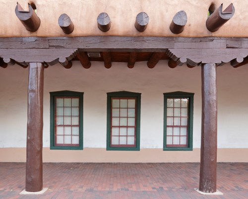 A rustic building with three windows and wooden beams, featuring a clay roof and brick flooring.