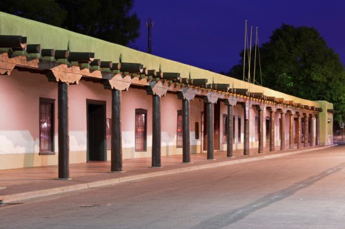 Historic building with wooden beams and columns, illuminated at dusk, along a quiet street.