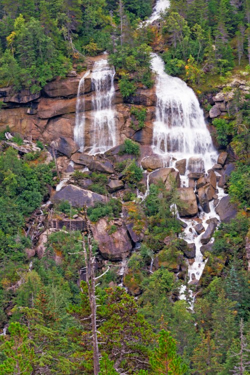 A scenic view of cascading waterfalls flowing down rocky cliffs, surrounded by lush green trees and vegetation.