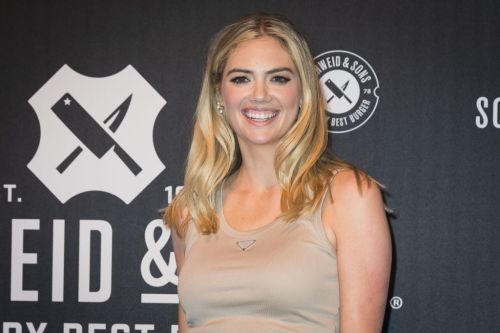 A smiling woman with long blonde hair poses in front of a dark backdrop featuring logos.