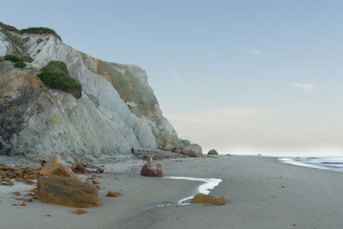 A serene beach scene with white cliffs, smooth sand, and gentle waves under a clear sky.