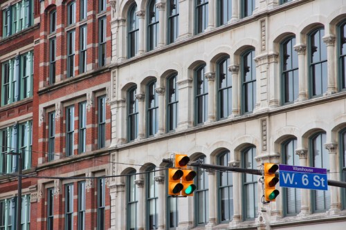Historic buildings with ornate windows and a traffic light at the intersection of W. 6 St. in an urban setting.