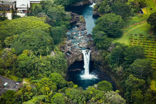 Aerial view of a lush green landscape featuring a waterfall cascading into a river surrounded by dense foliage.