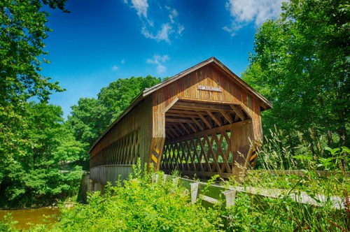 A wooden covered bridge surrounded by lush greenery under a bright blue sky.