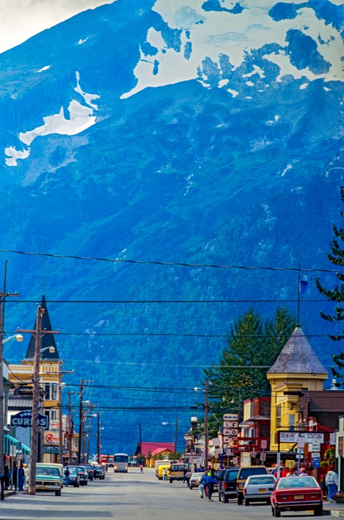 A scenic street view with shops and cars, framed by a towering snow-capped mountain in the background.