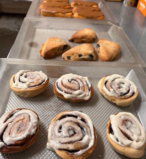 A tray of freshly baked pastries, including cinnamon rolls and scones, arranged on a metal surface.