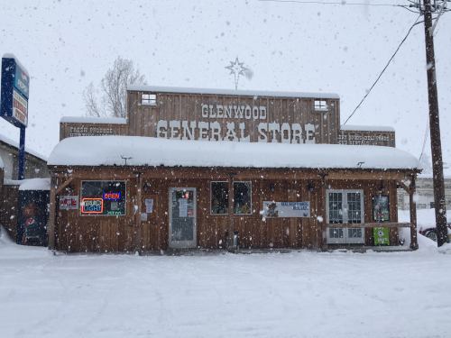 A wooden general store covered in snow, with a sign reading "Glenwood General Store" and colorful neon lights.