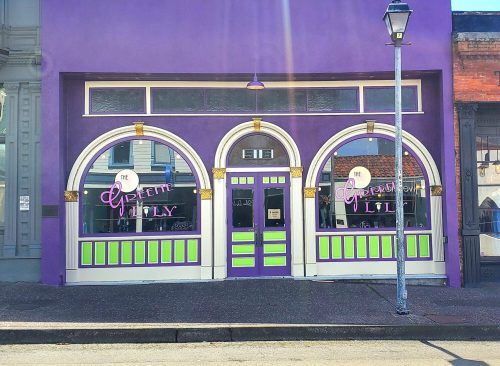 A vibrant purple storefront with green accents and large arched windows, featuring the name "Apreme Lily" in pink.