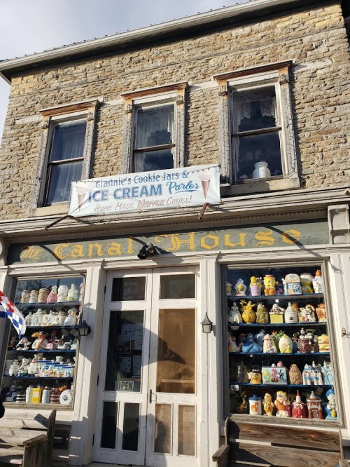 A stone building with a sign for ice cream and cookie jars, featuring colorful ceramic figurines in the windows.