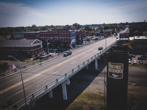 Aerial view of a bridge over a road with buildings and trees in the background, featuring a "Historic Richmond" sign.