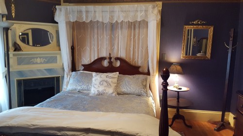 A cozy bedroom featuring a wooden bed with decorative bedding, a vintage mirror, and soft lighting.