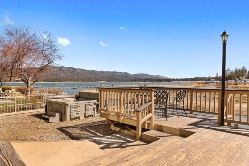 Scenic view of a lake with mountains in the background, featuring a wooden deck and outdoor seating.