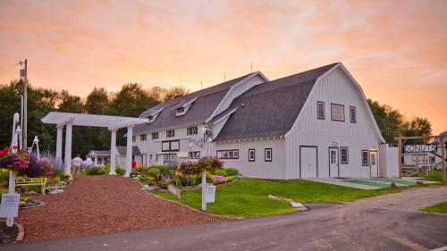 A charming white barn with a landscaped path and colorful flowers, set against a sunset sky.