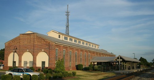 A brick building with a tower, next to a train platform and a police car, under a clear blue sky.