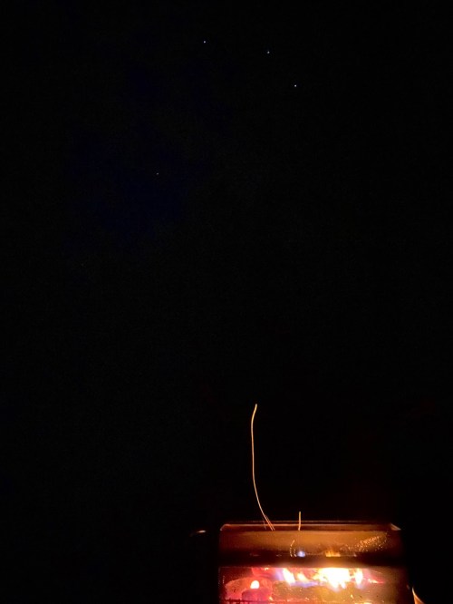 A glowing campfire in the foreground with a dark night sky and a few stars visible above.