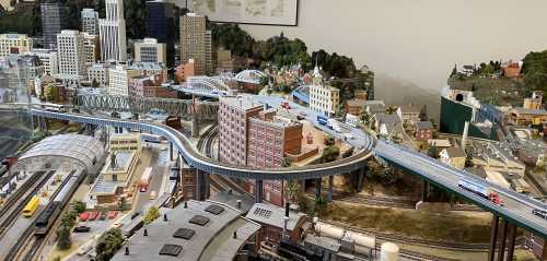 A detailed model train layout featuring buildings, roads, and tracks in a miniature cityscape.