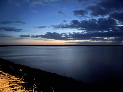 A serene lake at dusk, with a colorful sky and clouds reflecting on the water's surface.