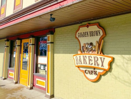 A colorful bakery café sign reading "Golden Brown Bakery" on a brick wall, with a welcoming storefront.