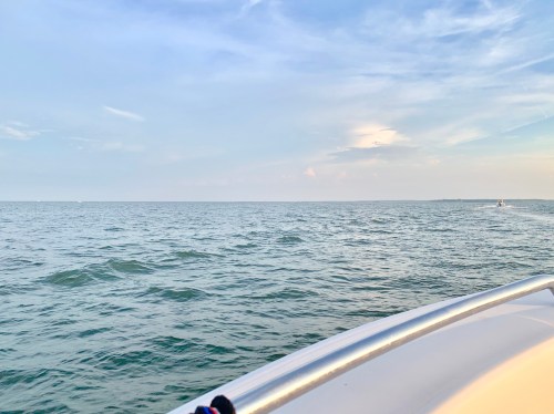A serene view of calm waters under a blue sky, seen from the side of a boat.