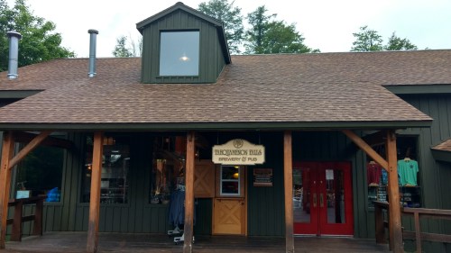 Exterior of a green brewery and pub with a wooden porch, featuring a sign and large red doors.