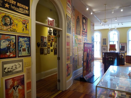 A hallway lined with colorful vintage posters and framed art, leading to an exit in a museum setting.