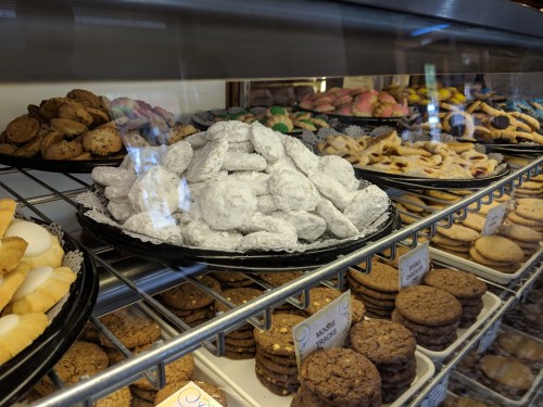 A display case filled with various cookies, including powdered sugar cookies, chocolate chip, and colorful iced treats.