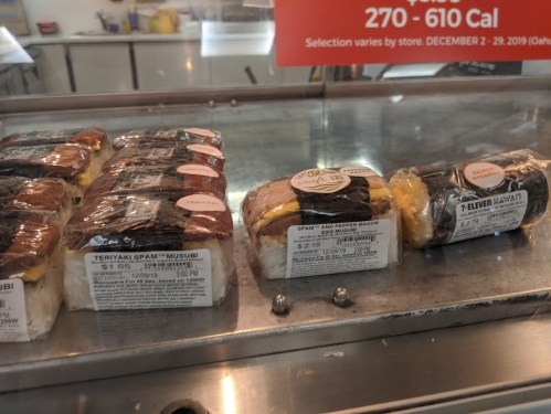 A display case with various musubi options, including teriyaki spam and spam with pepper bacon, with price tags visible.