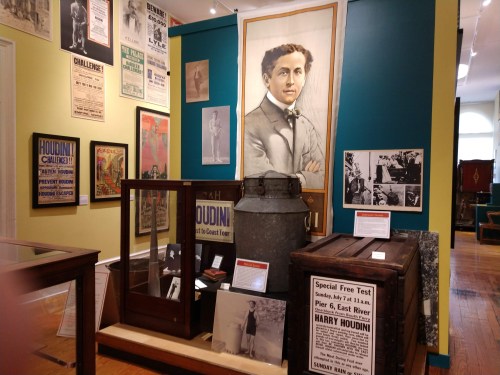 Exhibit featuring vintage posters, photographs, and artifacts related to Harry Houdini in a museum setting.