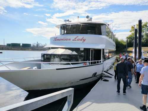 A white boat named "American Lady" docked at a marina with people boarding on a sunny day.