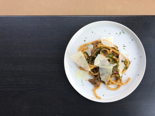 A plate of pasta topped with herbs and shaved cheese, served on a dark wooden table.