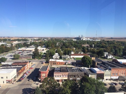 Aerial view of a small town with buildings, trees, and fields under a clear blue sky.