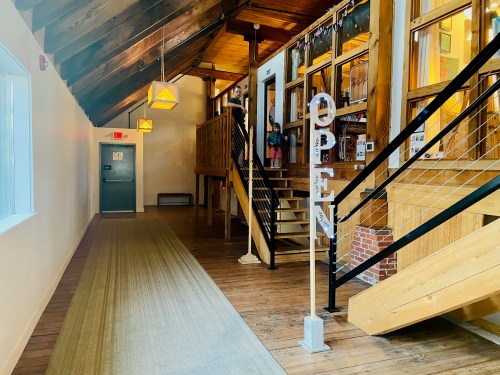 A bright hallway with wooden beams, an "OPEN" sign, and stairs leading to a second level.