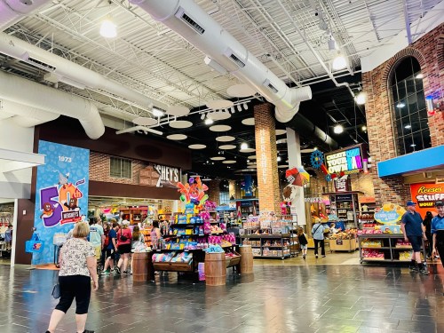 A colorful candy store interior with shelves of sweets, bright decorations, and shoppers browsing the aisles.